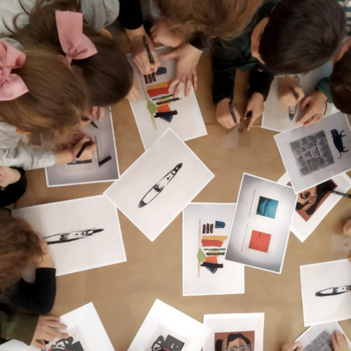 Vista superior de un grupo de niñas y niños coloreando reproducciones de obras de arte.
